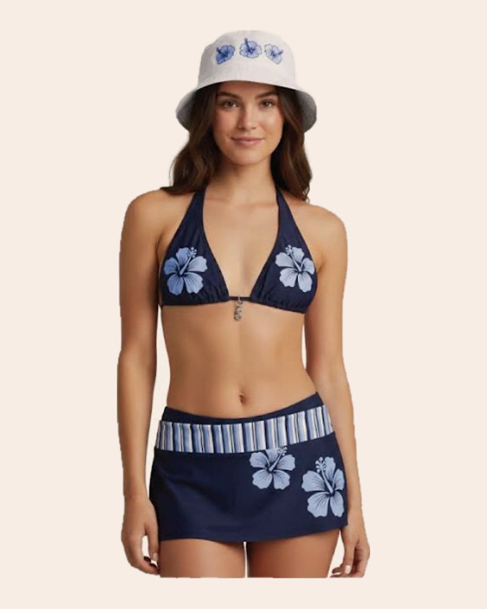 A model in a navy halter bikini top, matching swim skirt and a white bucket hat, all in a pale blue hibiscus print